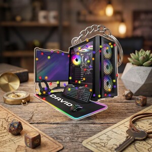 May include: An acrylic keychain featuring a gaming setup with a computer tower, monitor, keyboard, mouse, and headset. The desk mat displays the name DAVID. The entire scene is decorated with colorful string lights and includes a metal keyring attachment.