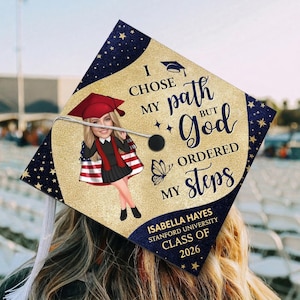 May include: A graduation cap with a gold glitter background and navy blue star-studded borders. The cap features the text "I chose my path but God ordered my steps." A cartoon image of a graduate is in the center. The graduate's name, university, and class year are also displayed.