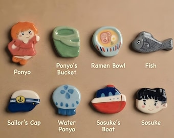 May include: A set of eight ceramic chopstick rests featuring various designs: a girl, a green bucket, a ramen bowl, a gray fish, a blue sailor's cap, a blue and white jellyfish, a red and white boat, and a boy's face, with labels below each.