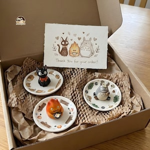 May include: A gift box containing three small ceramic plates with cartoon character figurines. The plates are decorated with food and nature-themed designs. A card with the text "Thank You for your order!" is also included.