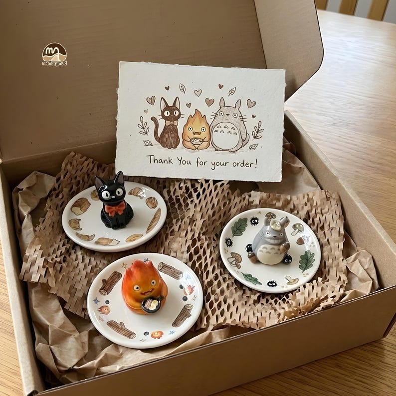 May include: A gift box containing three small ceramic plates with cartoon character figurines. The plates are decorated with food and nature-themed designs. A card with the text "Thank You for your order!" is also included.
