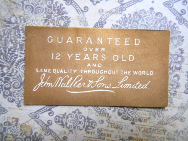 May include: A brown paper label with white text that reads "GUARANTEED OVER 12 YEARS OLD AND SAME QUALITY THROUGHOUT THE WORLD John Walker Sons Limited."
