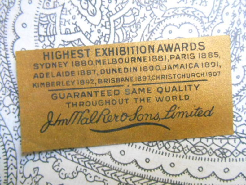 May include: A gold label with black text that reads "Highest Exhibition Awards" and lists cities and years. The text continues with "Guaranteed Same Quality Throughout the World" and "J.M. Hall & Sons, Limited".
