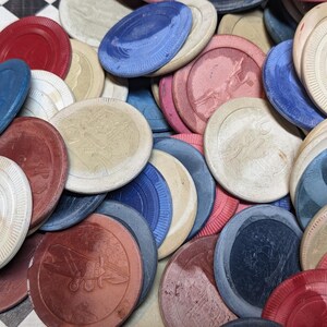 May include: A pile of vintage poker chips in various colors, including red, blue, white, and brown. The chips have a worn, distressed look, suggesting they have been used many times.