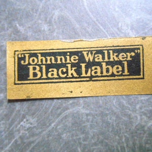 K&ouml;nnte beinhalten: Ein goldenes Etikett mit schwarzem Text, auf dem "Johnnie Walker" Black Label steht.