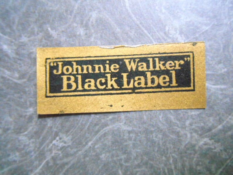 K&ouml;nnte beinhalten: Ein goldenes Etikett mit schwarzem Text, auf dem "Johnnie Walker" Black Label steht.