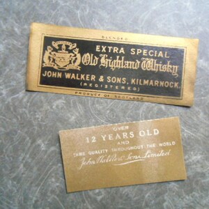 K&ouml;nnte beinhalten: Zwei Etiketten f&uuml;r eine Flasche Old Highland Whisky. Das obere Etikett ist schwarz mit goldenen Buchstaben und einem Wappen. Es lautet "Extra Special Old Highland Whisky John Walker & Sons, Kilmarnock (Registered) Produce of Scotland". Das untere Etikett ist golden mit wei&szlig;en Buchstaben und lautet "Over 12 Years Old and Same Quality Throughout the World John Walker & Sons Limited".