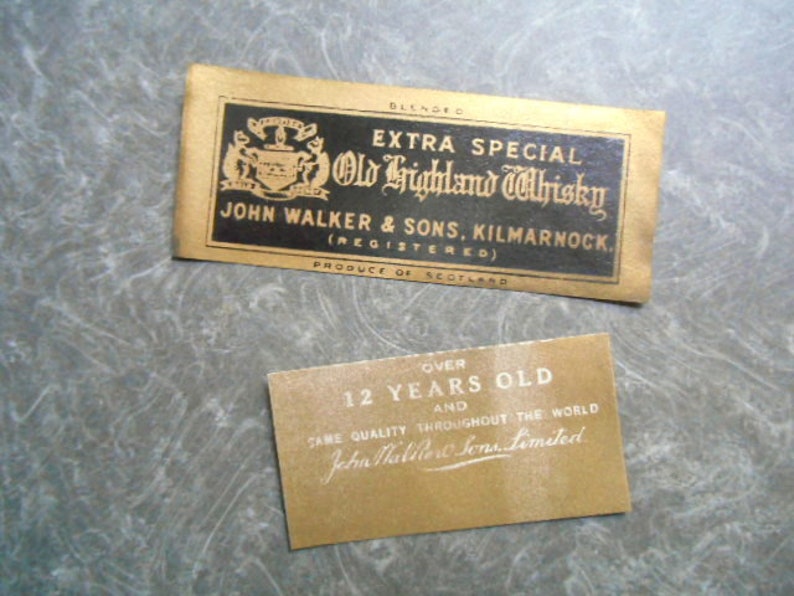 K&ouml;nnte beinhalten: Zwei Etiketten f&uuml;r eine Flasche Old Highland Whisky. Das obere Etikett ist schwarz mit goldenen Buchstaben und einem Wappen. Es lautet "Extra Special Old Highland Whisky John Walker & Sons, Kilmarnock (Registered) Produce of Scotland". Das untere Etikett ist golden mit wei&szlig;en Buchstaben und lautet "Over 12 Years Old and Same Quality Throughout the World John Walker & Sons Limited".