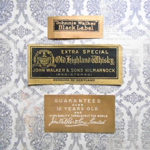 May include: Three vintage labels for Johnnie Walker Black Label Scotch Whisky. The labels are gold and black with white text. The top label reads "Johnnie Walker Black Label". The middle label reads "Extra Special Old Highland Whisky. John Walker & Sons Kilmarnock (Registered) Produce of Scotland". The bottom label reads "Guaranteed Over 12 Years Old and Same Quality Throughout the World John Walker & Sons Limited".
