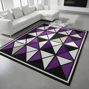 May include: A geometric area rug with a black border and a pattern of triangles in white, purple, black, and gray. The rug is rectangular and placed on a light gray floor in a modern living room setting.