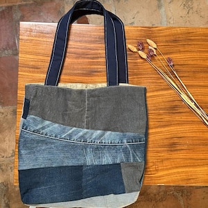 Peut inclure: Un sac fourre-tout en denim patchwork avec des anses bleu marine. Le sac est composé de différentes nuances de denim bleu, créant un aspect texturé et unique. Les anses sont bleu marine uni, offrant un contraste avec le corps en denim.