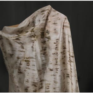 Puede incluir: Tela blanquecina con un patr&oacute;n de pinceladas marr&oacute;n oscuro y verde oliva. La tela est&aacute; drapeada, mostrando su textura y fluidez. El material parece ligero y adecuado para ropa o decoraci&oacute;n del hogar.