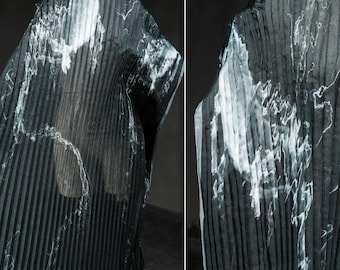 May include: A draped garment with vertical pleats, in shades of black and gray, with white marbled accents. The fabric appears semi-sheer, creating a flowing, textured effect. The garment is displayed on a stand, showcasing its design.