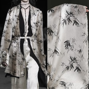 May include: A cream-colored kimono-style robe and matching fabric featuring a black bamboo leaf pattern. The robe has long sleeves and a belted waist. The fabric is held up to show the pattern.