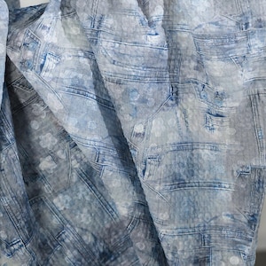 以下が含まれることがあります： 青とグレーの色合いのデニムプリントの生地。ポケット、縫い目、ボタン留めなどのディテールでジーンズの外観を模倣したデザイン。生地は折りたたまれ、影と奥行きを作り出しています。