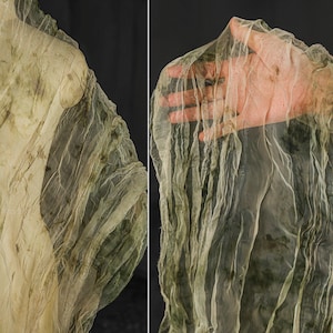 May include: Two-panel image of a translucent, textured fabric with a light green and beige color scheme. The fabric appears to be draped and folded, with darker green patches. The right panel shows a hand behind the fabric, visible through the material.