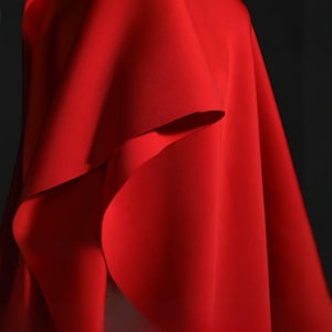 Könnte beinhalten: Nahaufnahme eines leuchtend roten Stoffes, der in weichen Falten drapiert ist. Die Textur des Stoffes ist glatt, mit subtilen Schatten, die Tiefe verleihen. Das Bild hebt die satte Farbe und die Art und Weise hervor, wie sich das Material drapiert.