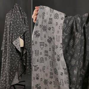 May include: Dark gray fabric with a repeating pattern of white Asian-inspired symbols. The fabric is draped over a form and held up by a hand, showcasing the design and texture. The fabric appears to be reversible.