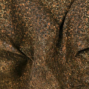 Puede incluir: Primer plano de una tela texturizada con un patrón moteado. El material es principalmente marrón con acentos de marrón claro y blanco, creando una apariencia natural y orgánica. La tela está doblada, mostrando profundidad y dimensión.