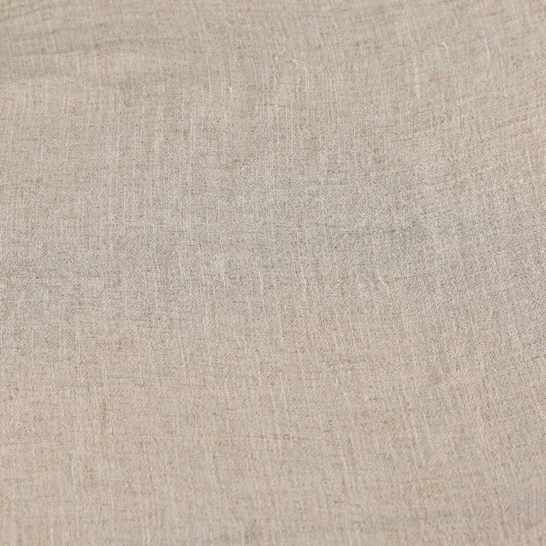 May include: Close-up of a beige linen fabric. The fabric has a textured surface with visible vertical and horizontal threads, creating a subtle grid pattern. The color is a neutral, light tan, suitable for various textile applications.