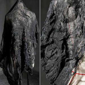 Può includere: Tessuto nero drappeggiato con una superficie strutturata e increspata. Il tessuto è esposto su un manichino, mostrando il suo design fluido e a strati. Un primo piano rivela i dettagli intricati e una sottile cucitura rossa.