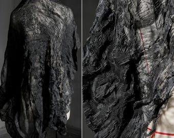 May include: A draped black textile with a textured, rippled surface. The fabric is displayed on a mannequin, showcasing its flowing, layered design. A close-up reveals the intricate details and a subtle red seam.