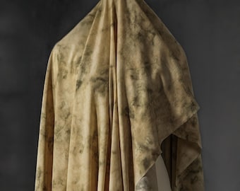 Puede incluir: Una tela drapeada con un patrón veteado en tonos beige y verde oliva. La tela está colgada, con pliegues y sombras que crean profundidad. El efecto general es de textura y tonos naturales.