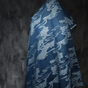 May include: A draped piece of blue fabric with a white cloud pattern. The fabric has a denim-like appearance and a textured surface. The cloud design is repeated across the material, creating a flowing, artistic effect. The fabric is likely used for clothing or home decor.