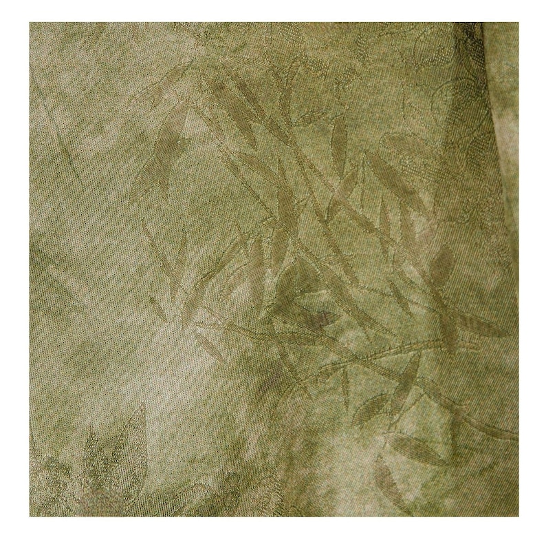 May include: Close-up of a textured fabric with a repeating leaf pattern in shades of olive green and tan. The fabric has a subtle sheen and a slightly mottled appearance, suggesting a natural fiber material.