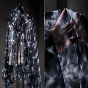 May include: A sheer, tie-dye fabric draped over a dress form. The fabric has a pattern of white and grey splotches against a dark background. The fabric is lightweight and appears to be flowing. The image is a close-up of the fabric.