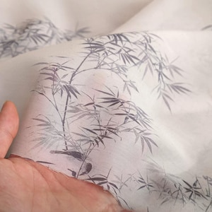 May include: Close-up of a sheer, off-white fabric with a delicate bamboo print in shades of grey. The design features detailed bamboo stalks and leaves, creating a serene, natural aesthetic. The fabric is slightly translucent, suggesting a lightweight material.
