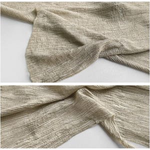 Puede incluir: Primer plano de una tela beige con una apariencia texturizada y arrugada. La tela est&aacute; doblada y drapeada, revelando el tejido detallado y sutiles variaciones de color. El material parece suave y ligero, adecuado para ropa o decoraci&oacute;n del hogar.