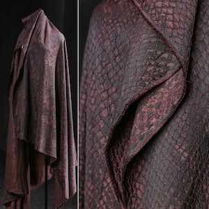 May include: A burgundy fabric with a snakeskin pattern is draped over a stand. The fabric has a textured surface and a dark red trim. The fabric is likely used for clothing or home decor.