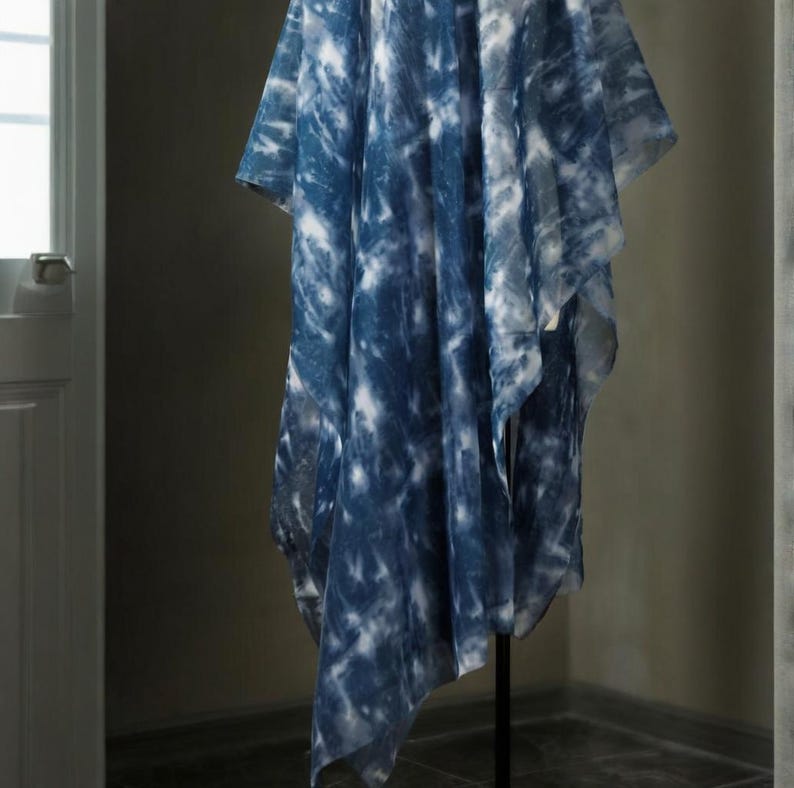 May include: A blue and white tie-dye patterned garment. The fabric is lightweight and has a loose, draped shape. The garment is displayed on a black stand, highlighting its design and texture. The garment's measurements are in centimeters.