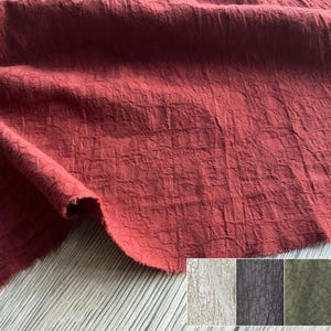 Puede incluir: Primer plano de una tela roja texturizada con un patrón similar a una cuadrícula. La tela está doblada, revelando su textura y variaciones de color. La imagen también muestra una paleta de colores de telas similares en blanco, gris y verde oliva.
