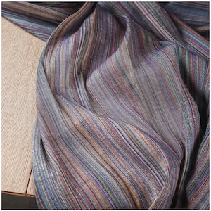 Puede incluir: Primer plano de una tela drapeada con rayas verticales en tonos azules, morados, marrones y rojos. La tela tiene un brillo sutil, lo que sugiere seda o satén. Las rayas varían en ancho, creando una apariencia texturizada.