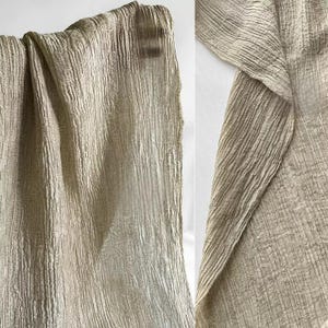 Puede incluir: Primer plano de una tela beige texturizada con l&iacute;neas verticales. La tela est&aacute; drapeada, mostrando pliegues y una superficie ondulada. El material parece suave y ligero, adecuado para ropa o decoraci&oacute;n del hogar.