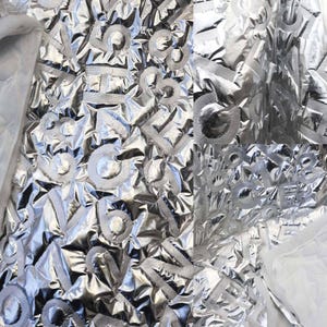 Peut inclure: Gros plan sur un tissu argenté brillant avec des chiffres et des lettres blancs en relief. Le tissu est froissé, créant une surface texturée. Les chiffres et les lettres semblent être placés au hasard.