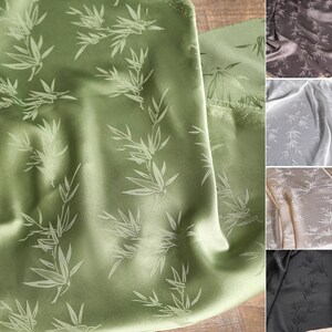 May include: Close-up of green fabric with a bamboo leaf pattern. The fabric has a satin sheen and is folded, revealing the texture and design. Additional fabric swatches in shades of gray, brown, and black are visible.