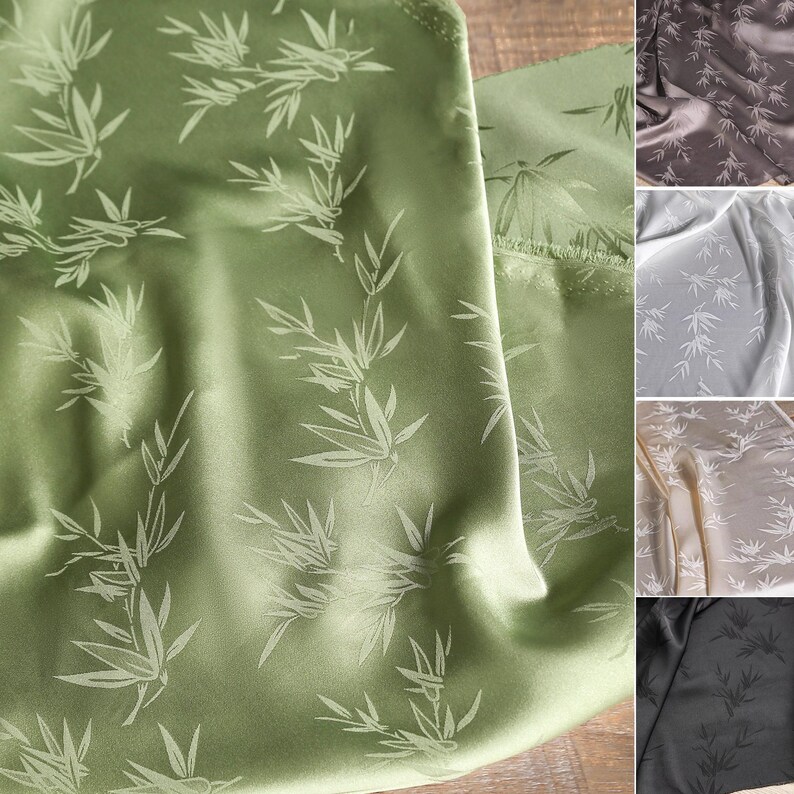 May include: Close-up of green fabric with a bamboo leaf pattern. The fabric has a satin sheen and is folded, revealing the texture and design. Additional fabric swatches in shades of gray, brown, and black are visible.