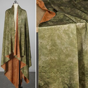 May include: Reversible shawl with a botanical print. The outer layer is olive green with a subtle floral pattern, while the reverse side is a warm, rust-colored fabric. The shawl is draped over a mannequin, showcasing its flowing design.