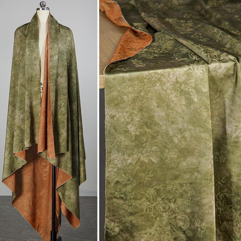 May include: Reversible shawl with a botanical print. The outer layer is olive green with a subtle floral pattern, while the reverse side is a warm, rust-colored fabric. The shawl is draped over a mannequin, showcasing its flowing design.
