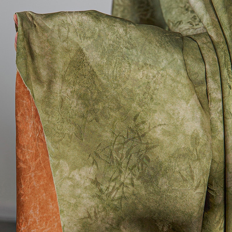 May include: Close-up of a green fabric with a textured, botanical pattern. The fabric has a layered appearance, with a rust-colored material visible beneath the green. The green fabric has a faded, vintage look.