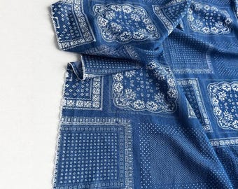 May include: A close-up of a blue fabric with a white paisley pattern. The fabric is folded, revealing a detailed design of squares and borders. The fabric has a soft, textured appearance, suitable for apparel or home decor.