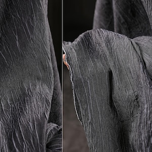 Könnte beinhalten: Nahaufnahme eines dunkelgrauen Stoffes mit strukturierter, zerknitterter Optik. Der Stoff hat vertikale und diagonale Linien, die ein einzigartiges Muster erzeugen. Die Kanten des Stoffes sind sichtbar und zeigen einen rohen, unfertigen Rand.