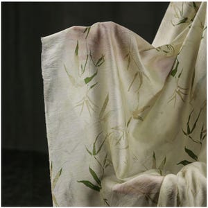 Puede incluir: Tela blanquecina con un delicado estampado de hojas de bambú en tonos verdes y beige. La tela es translúcida y fluida, con textura y pliegues visibles. El diseño evoca una estética natural y orgánica.