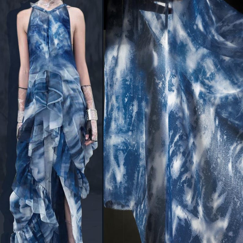 May include: A flowing, sleeveless dress in shades of blue and white, with a watercolour-like pattern. The dress has a halter neckline and layered ruffles, creating a dynamic silhouette. The fabric appears lightweight and airy, with a high slit.