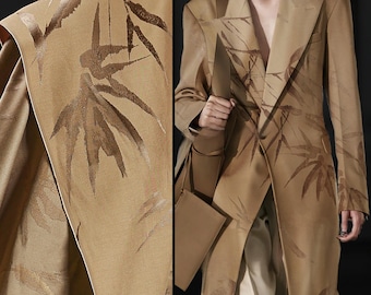 May include: A tan-colored long coat with a bamboo leaf pattern. The coat has a tailored design with a notched lapel and a single-button closure. The bamboo leaf design is in shades of brown and gold.