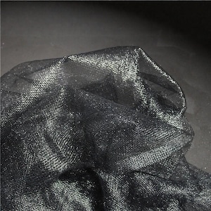 May include: Close-up of a black, shimmering fabric with a mesh-like texture. The fabric is folded and draped, creating shadows and highlights. The material appears to be lightweight and possibly used for apparel or decorative purposes.