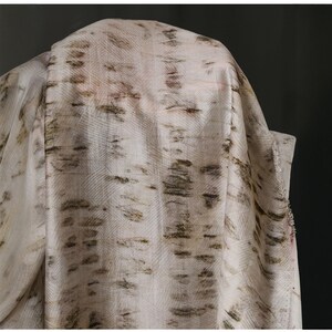 Puede incluir: Tela blanquecina con un dise&ntilde;o de corteza de abedul en tonos marrones y verdes. La tela est&aacute; drapeada, mostrando su textura y patr&oacute;n. El material parece ligero, adecuado para ropa o decoraci&oacute;n del hogar.